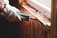 Crop unrecognizable workman in glove applying caulk from bottle on seam during window montage work in building