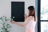 Back view of young female with long hair attaching empty rectangular frame on wall